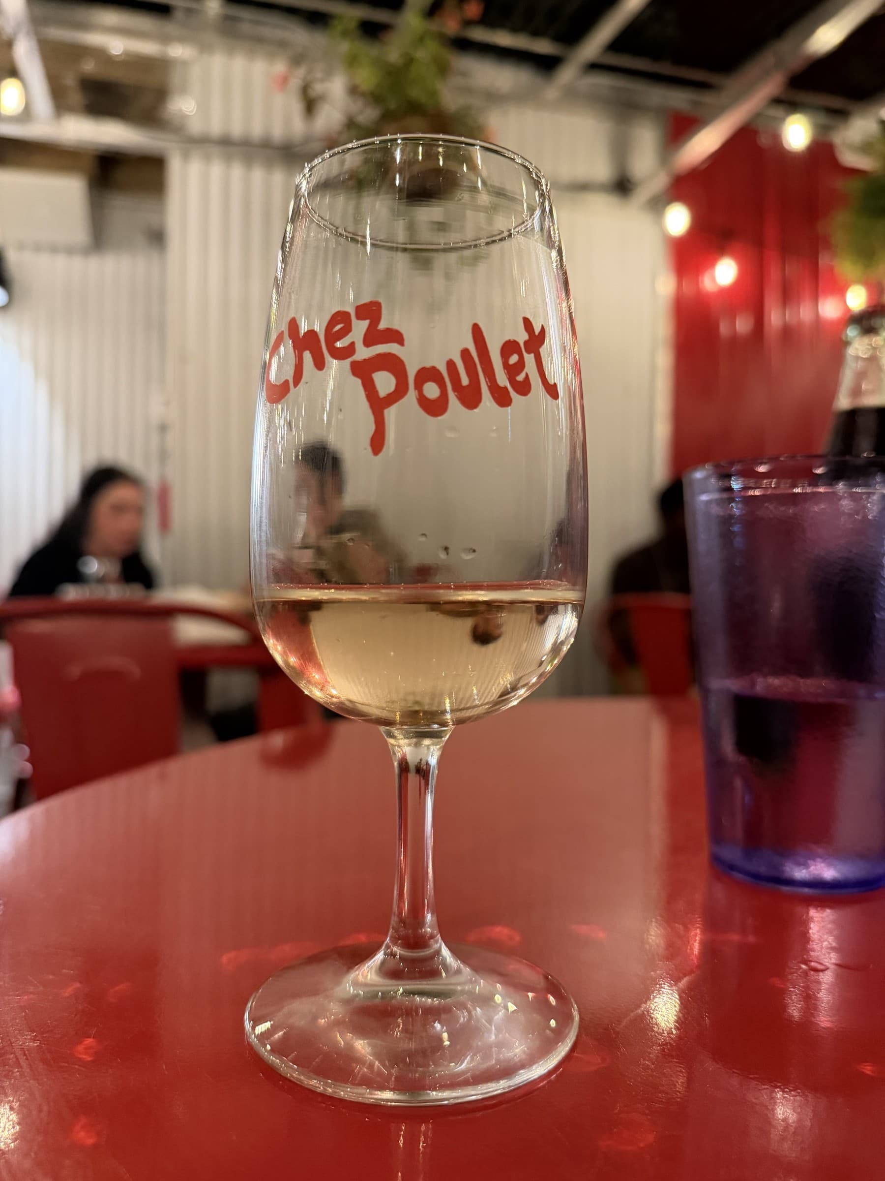 A Chez Poulet glass and red tabletop, photographed August 27, 2026. The wine is not identified.