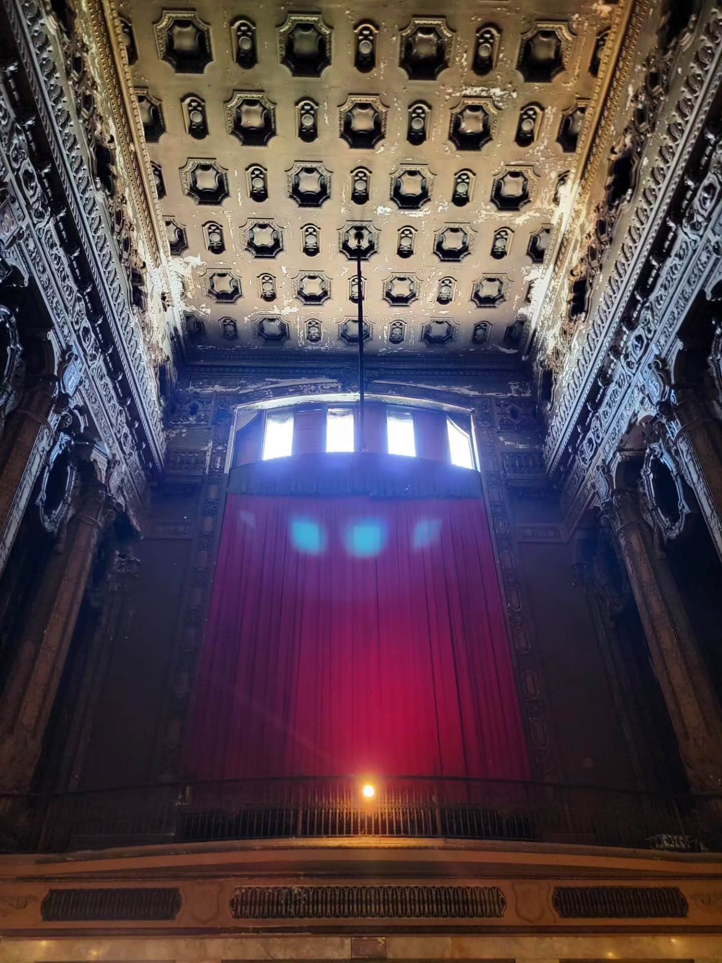 Looking up at a coffered, heavily ornamented ceiling above a tall red curtain inside the Uptown Theatre.
