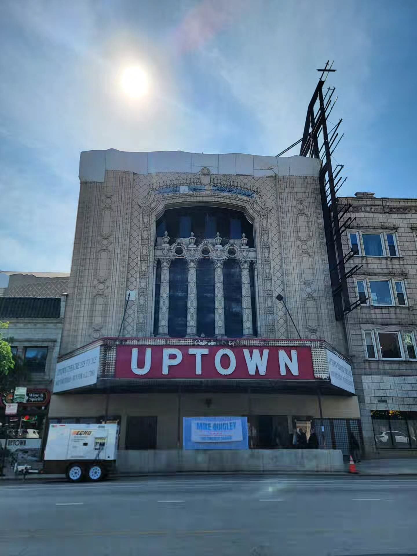 The Uptown Theatre's ornate facade, with a red UPTOWN marquee and a tall arched window, seen from across Broadway.